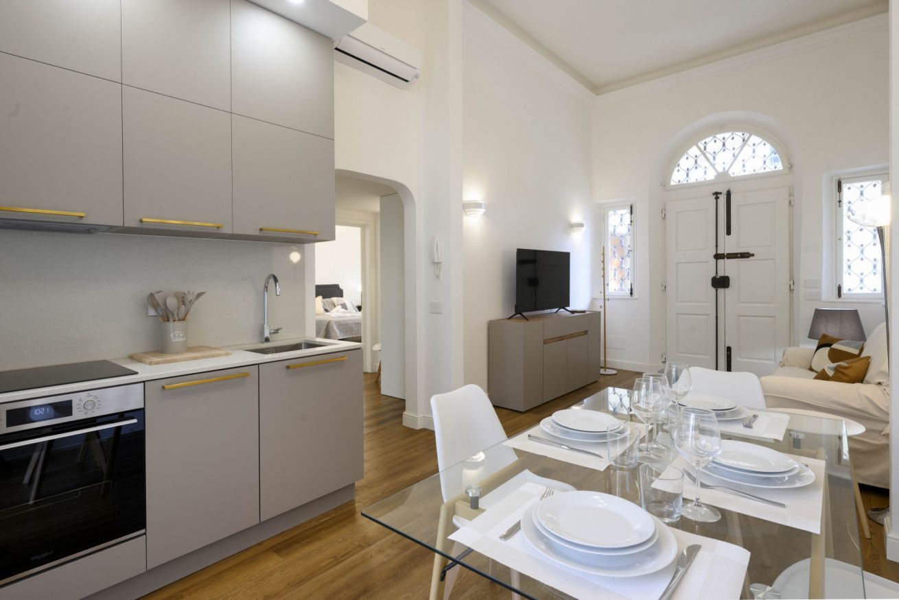 Una cucina moderna con mobili bianchi, forno integrato e zona pranzo con tavolo in vetro apparecchiata per sei.