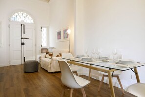 A dining area with a glass table, white chairs, and a sofa.
