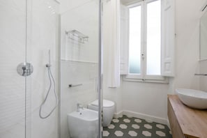 A modern bathroom with a glass shower enclosure, a white toilet, and a wooden vanity with a large sink.