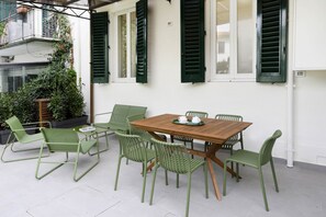 A patio with a wooden table and green chairs, surrounded by white walls and green shutters. - Hidden Gem with Private Garden (Firenze)