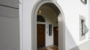 An arched entrance to a building with two wooden doors, numbered 7 and 9, and a small window with a metal grille. - Hidden Gem with Private Garden (Firenze)