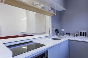 A modern kitchen with a built-in dishwasher, a stainless steel sink, and a wooden shelf above the countertop.