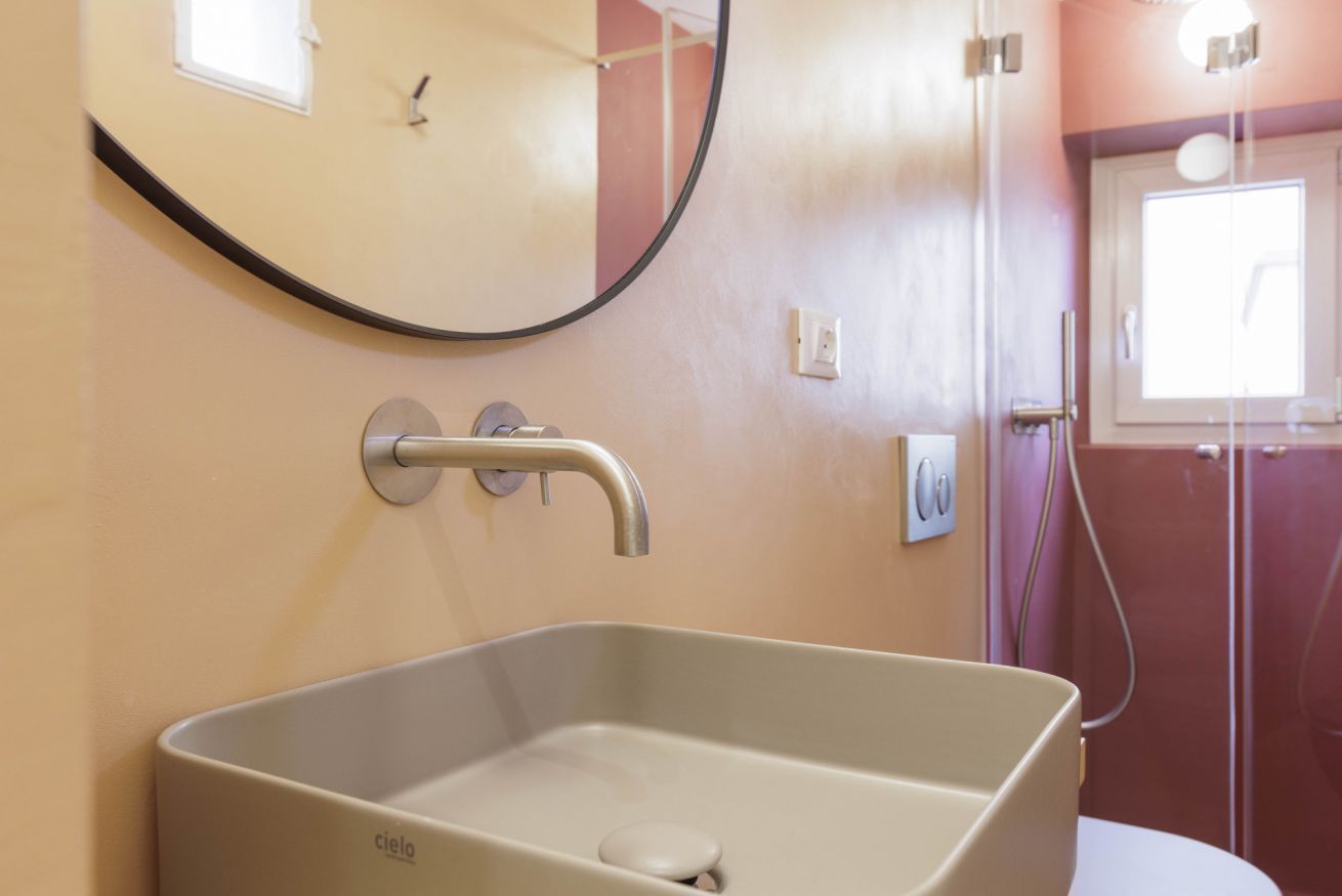 Un bagno con un lavandino rettangolare, uno specchio rotondo e una finestra.