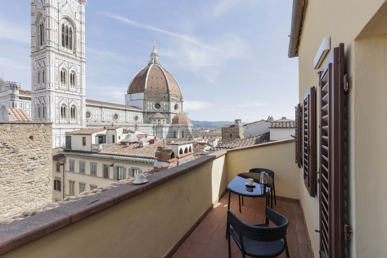 Un balcone con tavolo e sedie, affacciato su un edificio storico con una cupola e un campanile.