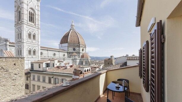 A balcony with a table and chairs, overlooking a historic building with a dome and a bell tower.