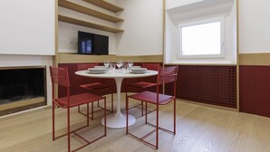 A dining area with a round table, red chairs, and a television on a shelf.