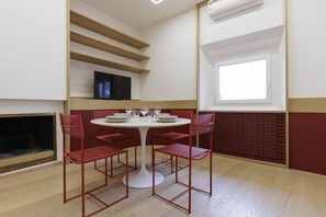Un comedor con una mesa redonda, sillas rojas y un televisor en un estante.