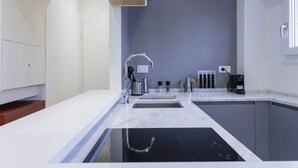 Eine moderne Küche mit schwarischem Kochfeld, weißen Arbeitsflächen und einer grauen Spritzschutzwand.