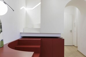 A modern interior with a curved red bench, a white wall with a light fixture, and a door in the background.