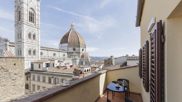 Ein Balkon mit Tisch und Stühlen, mit Blick auf ein historisches Gebäude mit Kuppel und Glockenturm.