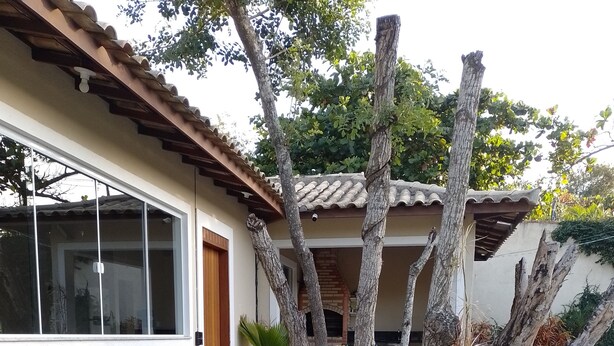 A swimming pool with a tiled deck, lounge chairs, and a pergola with trees. - Búzios Geribá beach house (Búzio)