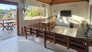 A spacious room with a wooden ceiling, a dining area with a table and chairs, a sofa, and a TV mounted on the wall. - Búzios Geribá beach house (Búzio)