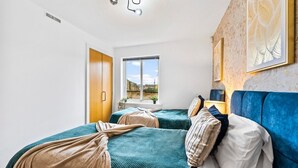 Ein Zimmer mit zwei Betten, einem Fenster, einer Tür und einer wandmontierten Lampe.