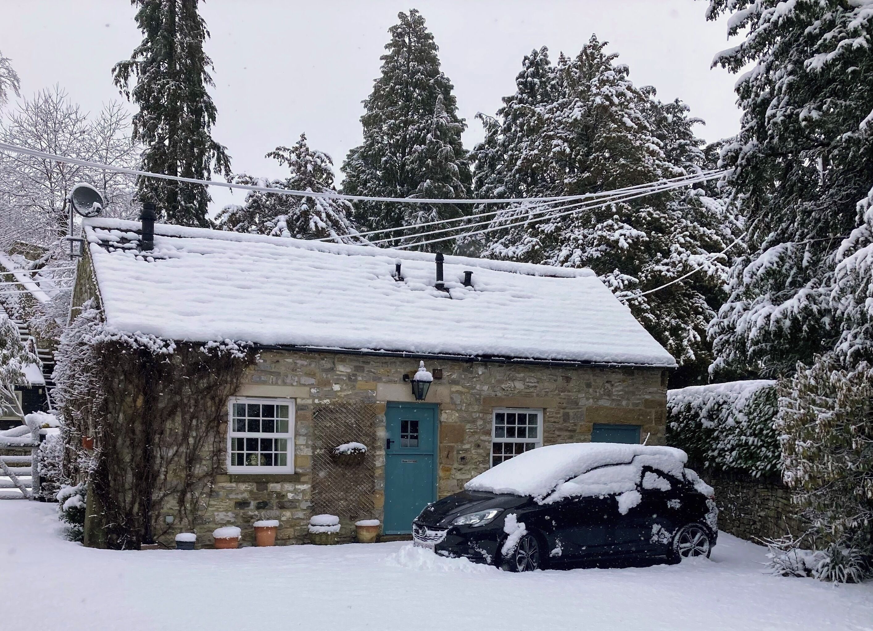 A stone cottage with a snow-covered roof, a blue door, and a car parked in front.