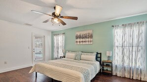 A bedroom with a large bed, a ceiling fan, a window with blinds, a bedside table with a lamp, and a painting on the wall. - Pool Home in SW Florida. 4 bedrooms,2 bathrooms, close to shopping and beaches. (North Port)