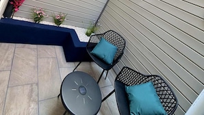 A patio with two black chairs and a small table, surrounded by a low wall with a blue base and pink flowers. - La Mandragore (Calais)