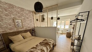 A bedroom with a bed, a brick wall, a mirror, and a hanging light fixture. - La Mandragore (Calais)