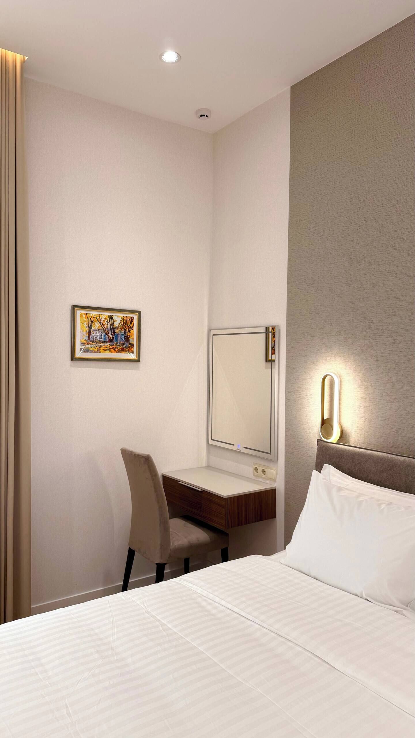 Une chambre d’hôtel avec un lit, un bureau, une chaise, un miroir et un tableau au mur.