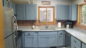 Una cocina con armarios azules, un refrigerador de acero inoxidable, un microondas y una ventana con vistas a árboles.