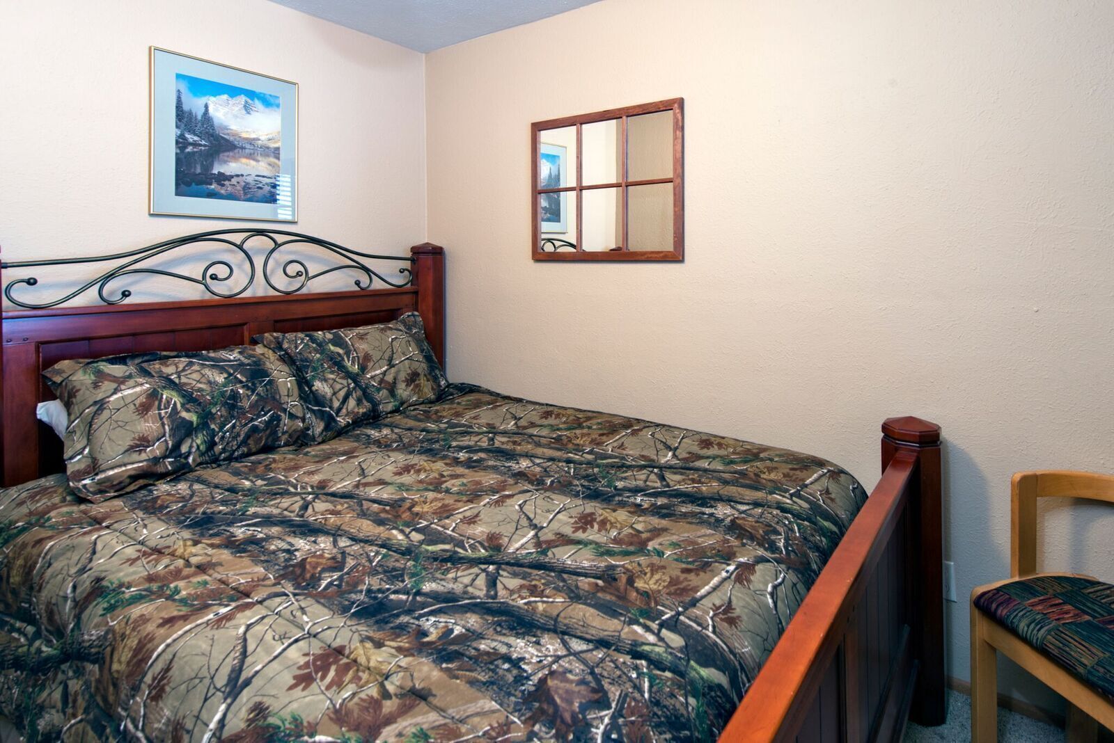 A bedroom with a bed, a wooden headboard, a chair, a framed picture, and a mirror on the wall.
