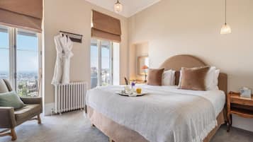 A hotel bedroom with a large bed, a view of the city, a sitting area with a chair, and a radiator.