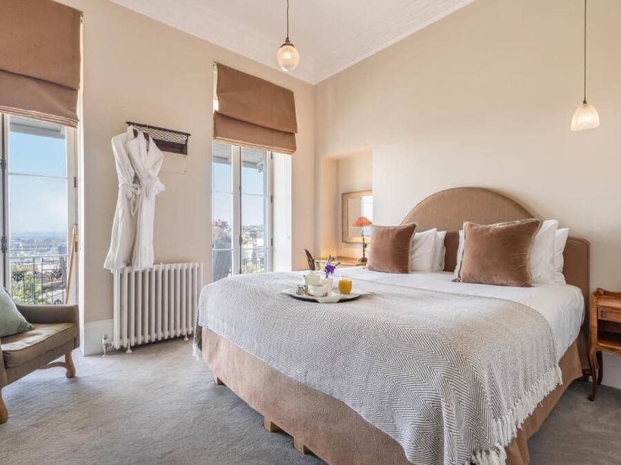A hotel bedroom with a large bed, a view of the city, a sitting area with a chair, and a radiator.