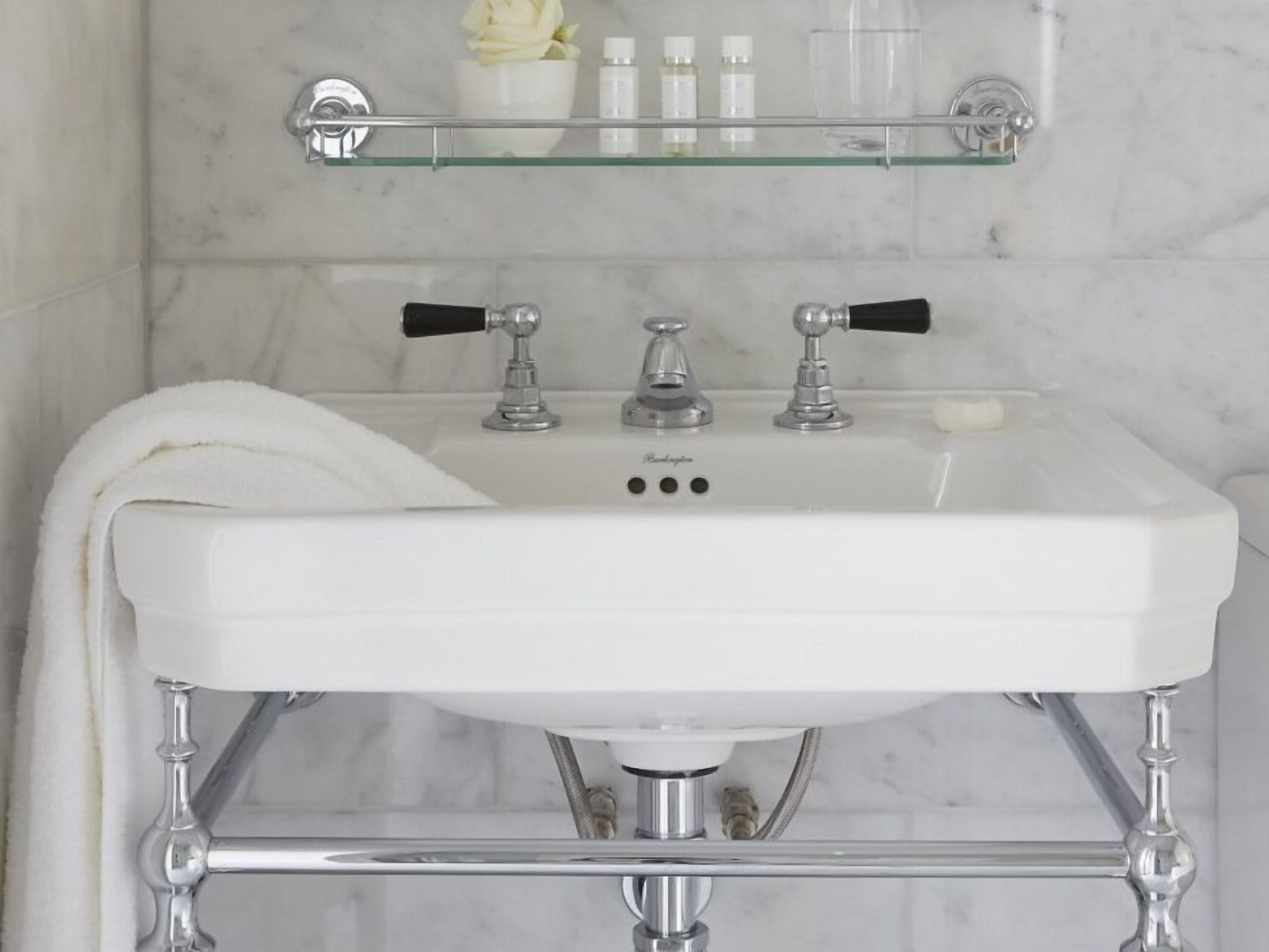 A bathroom with a white sink, chrome fixtures, and a glass shelf above the mirror.