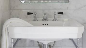 A bathroom with a white sink, chrome fixtures, and a glass shelf above the mirror.