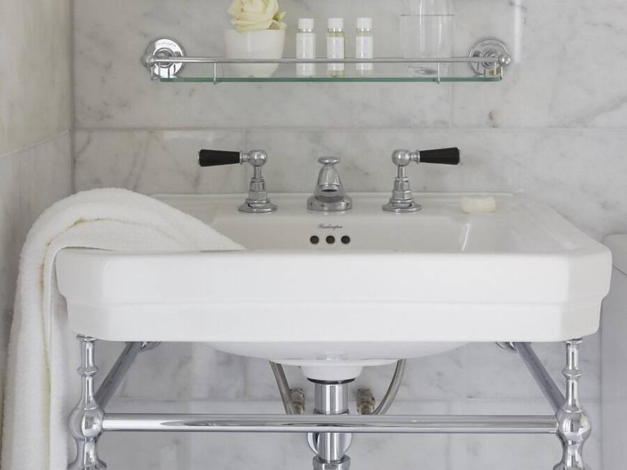 A bathroom with a white sink, chrome fixtures, and a glass shelf above the mirror.