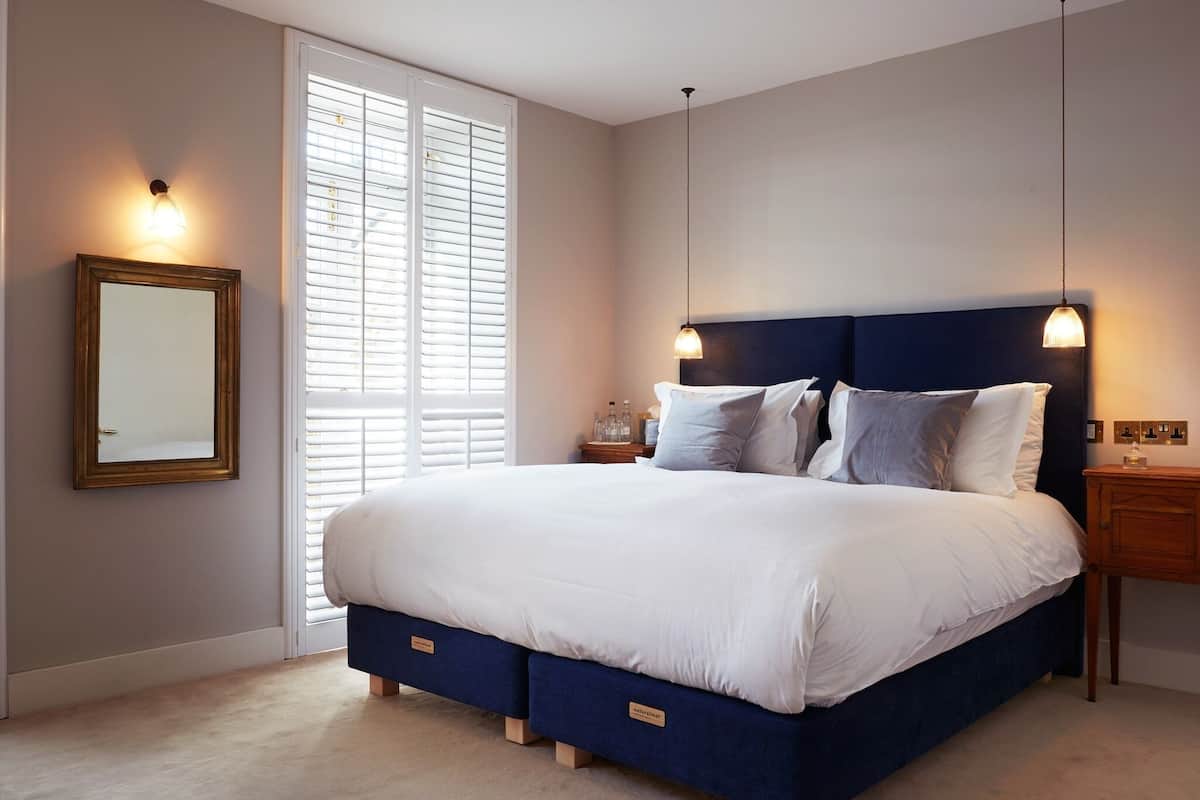 A bedroom with a large bed, a nightstand, a dresser, a mirror, and a window with blinds.
