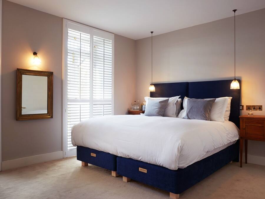 A bedroom with a large bed, a nightstand, a dresser, a mirror, and a window with blinds.