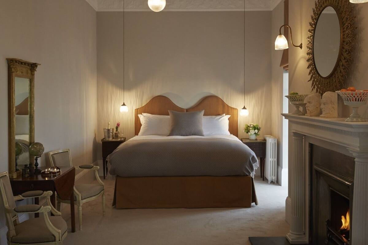 A bedroom with a large bed, two bedside tables, a mirror, a fireplace, and a chandelier.