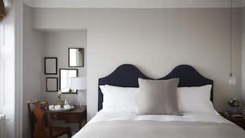 Un dormitorio ordenado con una cama grande, una mesita de noche con lámpara, una silla y un escritorio con espejo y un florero.