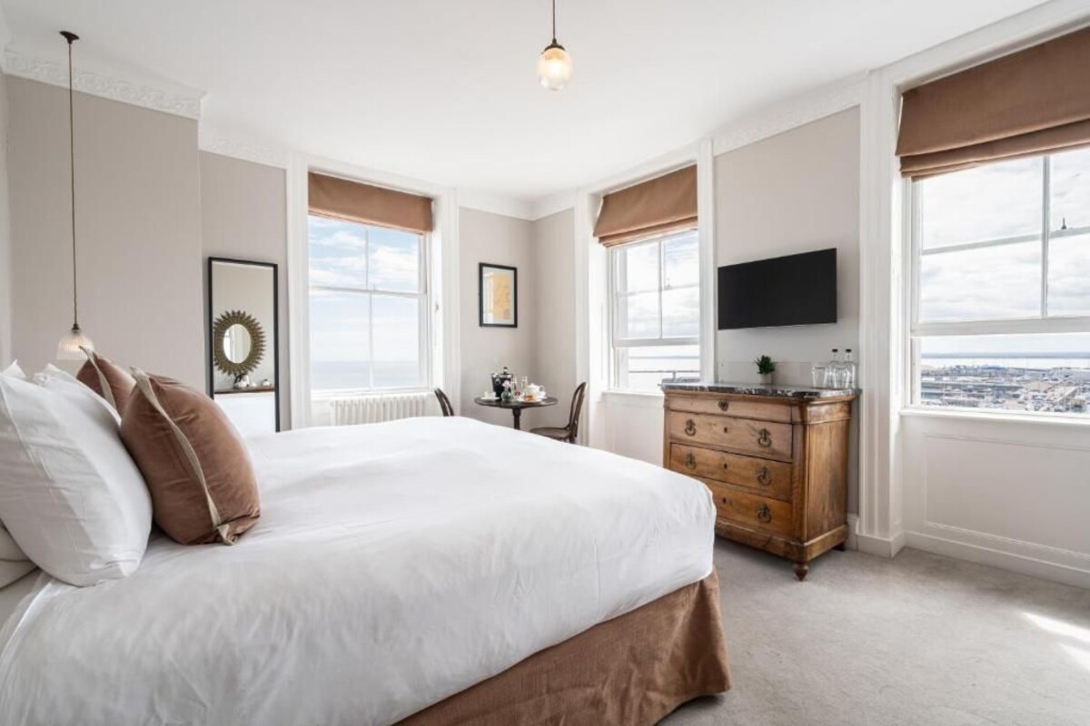 A bedroom with a large bed, a dresser, a chair, a television, and large windows with views.