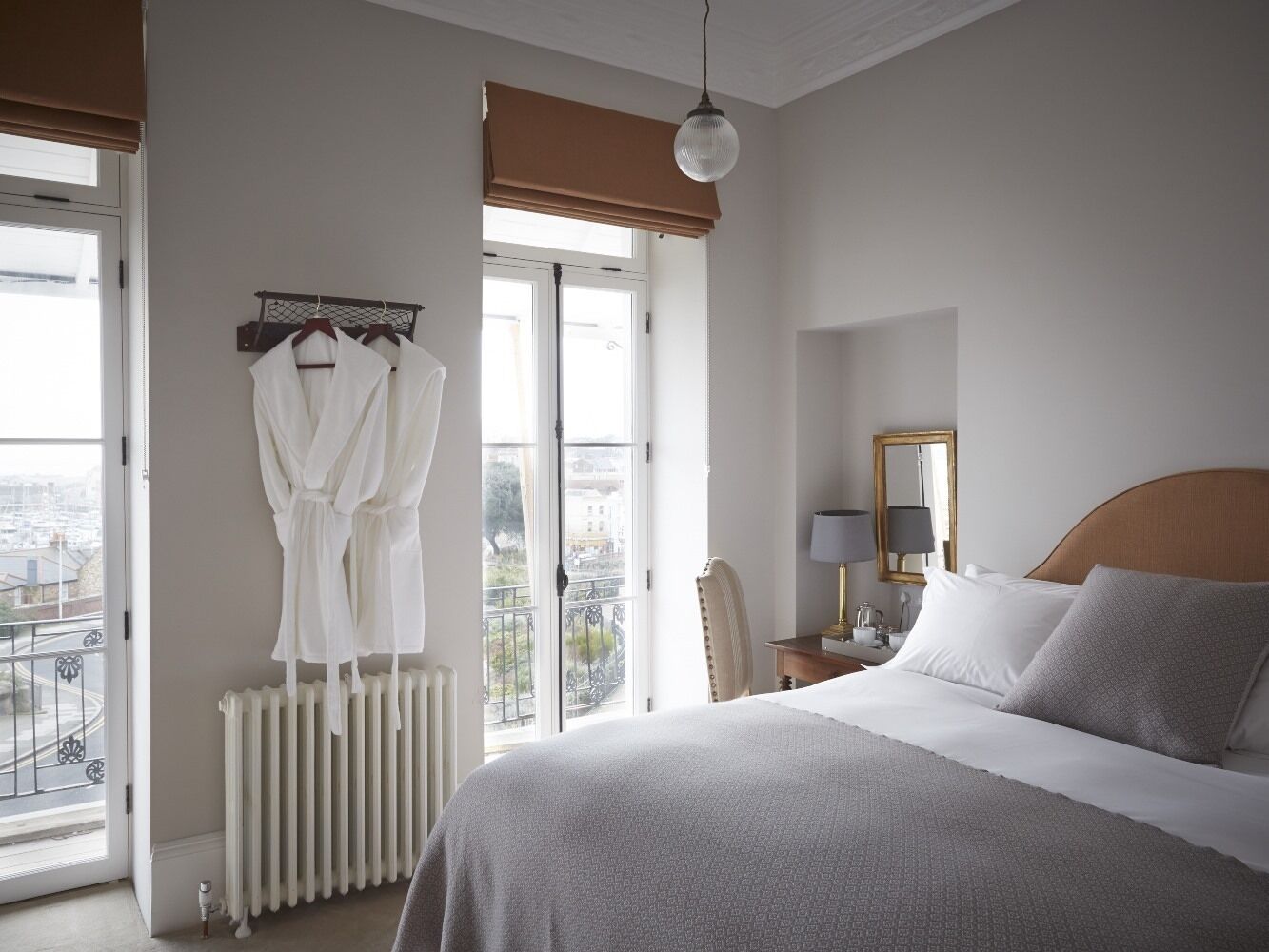 Ein Hotelzimmer mit einem großen Bett, einem Heizkörper, einem Sessel, einem Schreibtisch mit Lampe sowie einem Fenster mit Blick auf die Stadt.