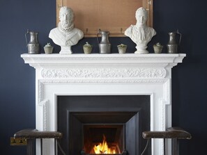A fireplace with two busts on the mantel, surrounded by three metal pitchers and three small potted plants. - The House at Ramsgate (Ramsgate)