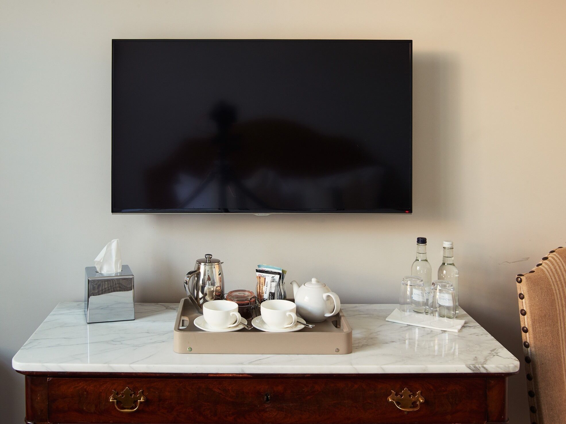 A hotel room with a marble countertop, a tray with cups and a teapot, a tissue box, and a bottle of water.