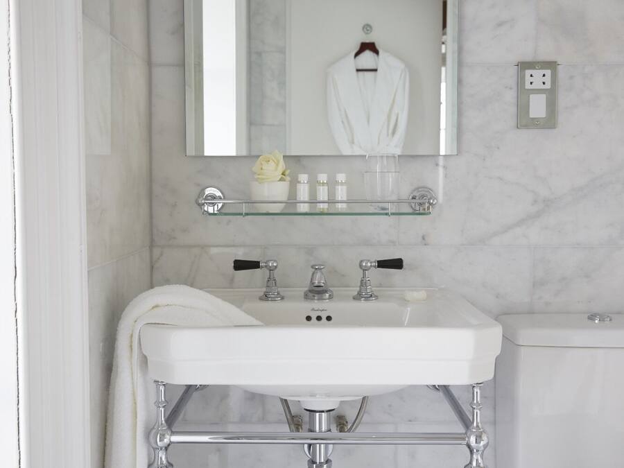 A bathroom with a white sink, a mirror, and a glass shelf above the sink.