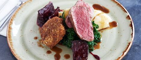 Une assiette de nourriture comprenant une tranche de viande, un aliment frit en forme de galette et des légumes verts, le tout servi dans une assiette en céramique.