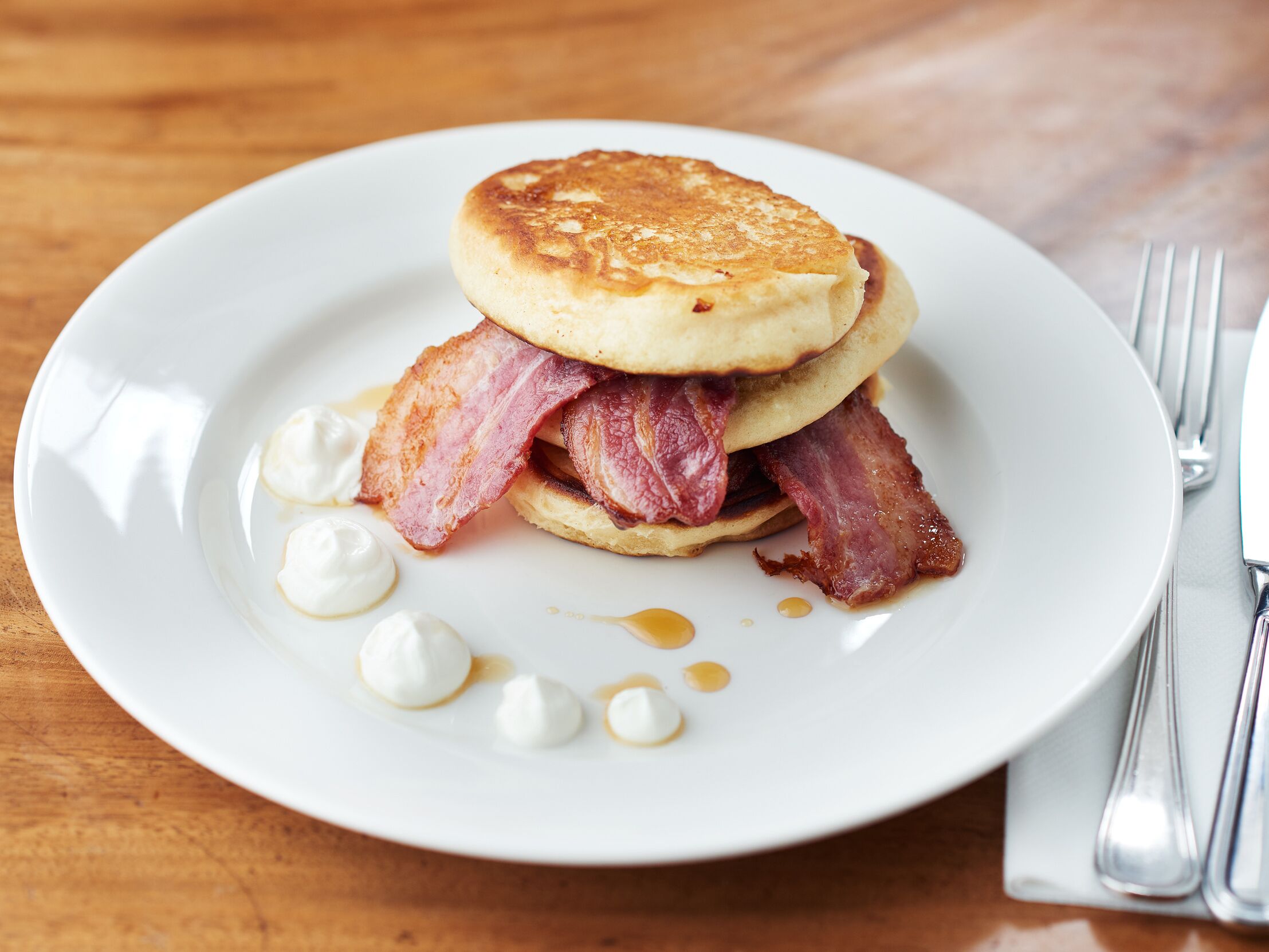 Un piatto per la colazione con pancake, pancetta e panna montata.