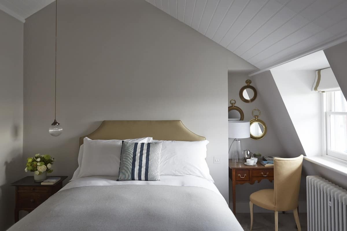 A bedroom with a bed, bedside table, lamp, chair, radiator, and decorative mirrors.