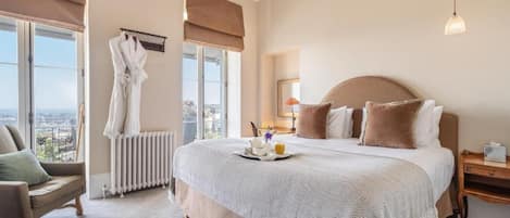 Et hotelværelse med en stor seng, udsigt over byen, et siddeområde med en stol og en radiator.