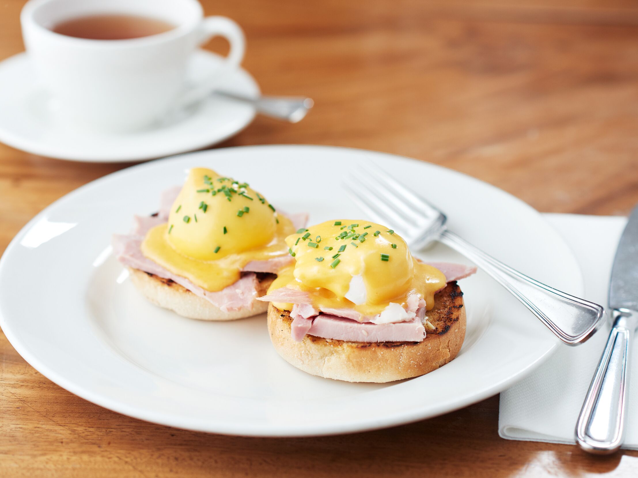 A plate with two eggs benedict sandwiches and a cup of coffee on a wooden table.
