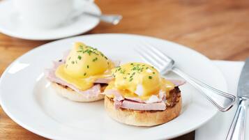 A plate with two eggs benedict sandwiches and a cup of coffee on a wooden table.