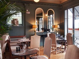 A dining area with round tables, cushioned chairs, and a large window providing natural light.
