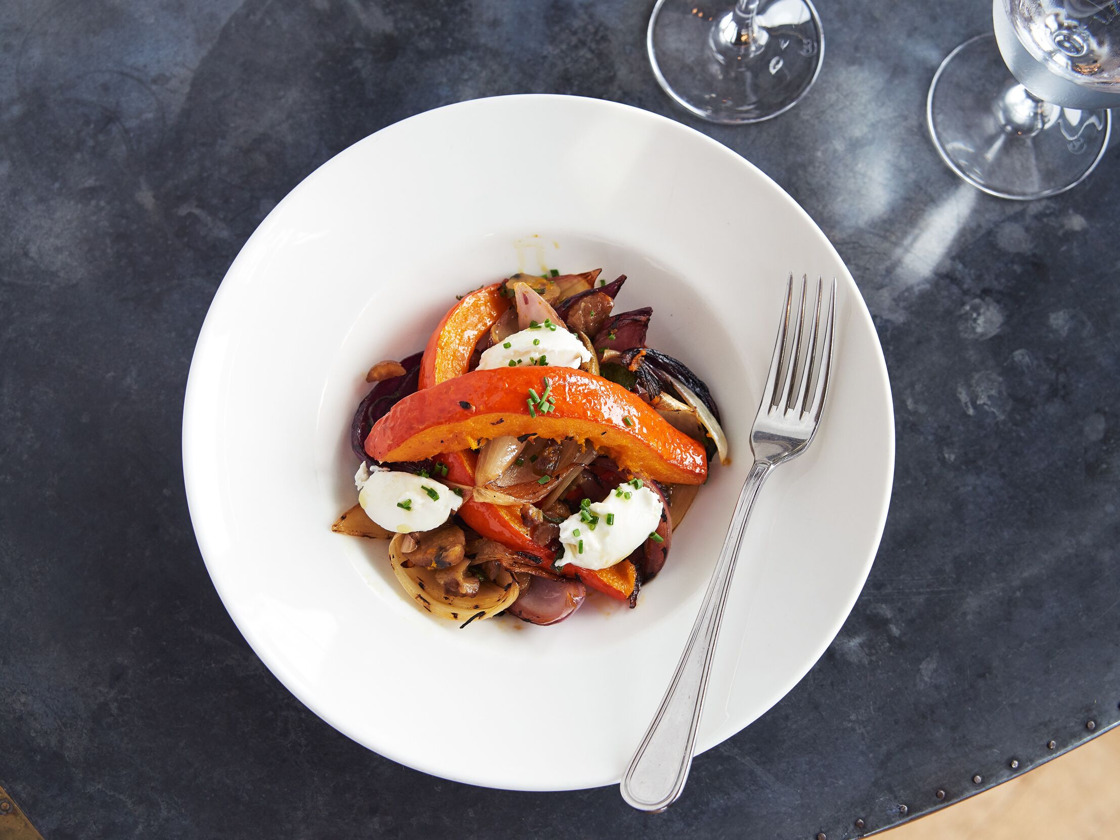 A white plate with a salad on a dark table.
