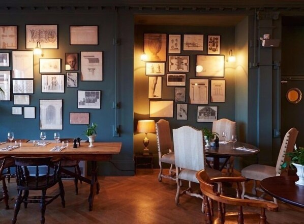 A dining area with a long wooden table and chairs, surrounded by walls adorned with framed architectural drawings and sketches.