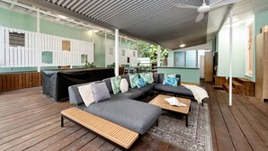 A modern outdoor lounge area with a wooden deck, grey sofas, and a ceiling fan. - Welcome to The Island House (Arcadia)