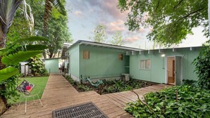 A green house with a wooden deck, surrounded by lush greenery and a small garden. - Welcome to The Island House (Arcadia)