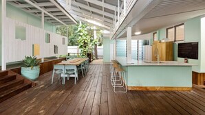 A spacious indoor area with a wooden floor, a long table with chairs, a bar area with stools, and a kitchen with a sink and cabinets. - Welcome to The Island House (Arcadia)